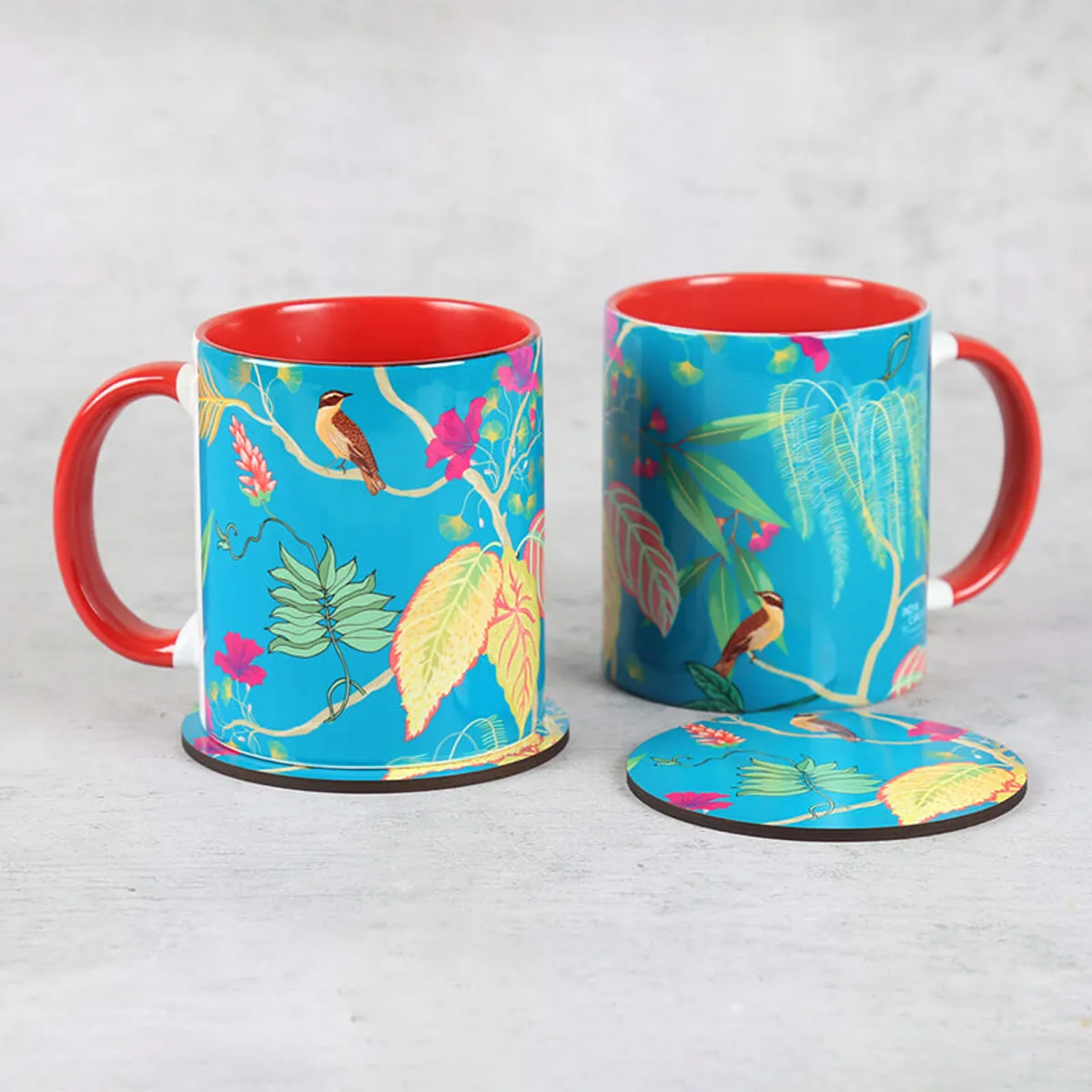 Two tropical blue ceramic mugs with red interiors and matching round coasters