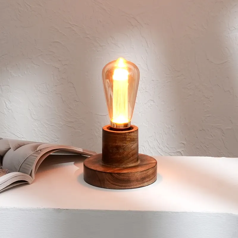 Brown wooden table lamp with glowing bulb placed beside an open book