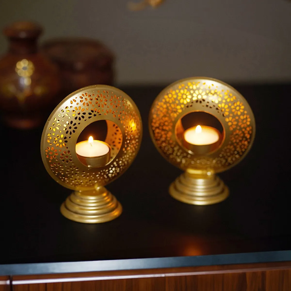 Two gold ornate tealight holders glowing in a dark setting