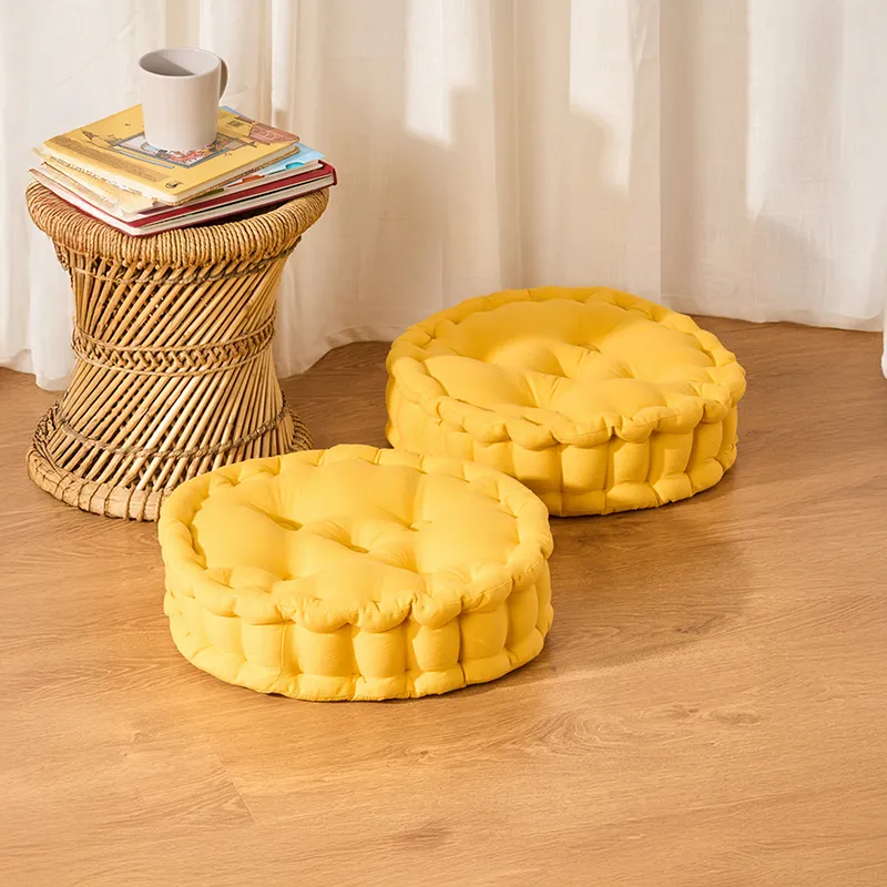 Two round mustard yellow floor cushions on a wooden floor beside a wicker side table