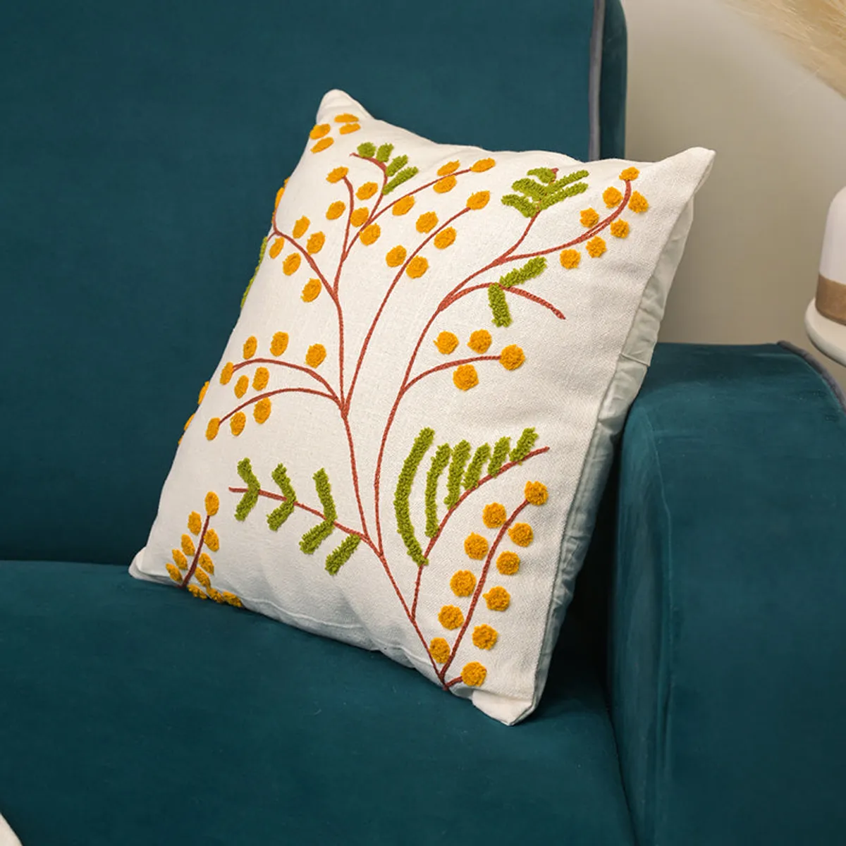 Angled view of ivory floral cushion cover placed on a teal armchair