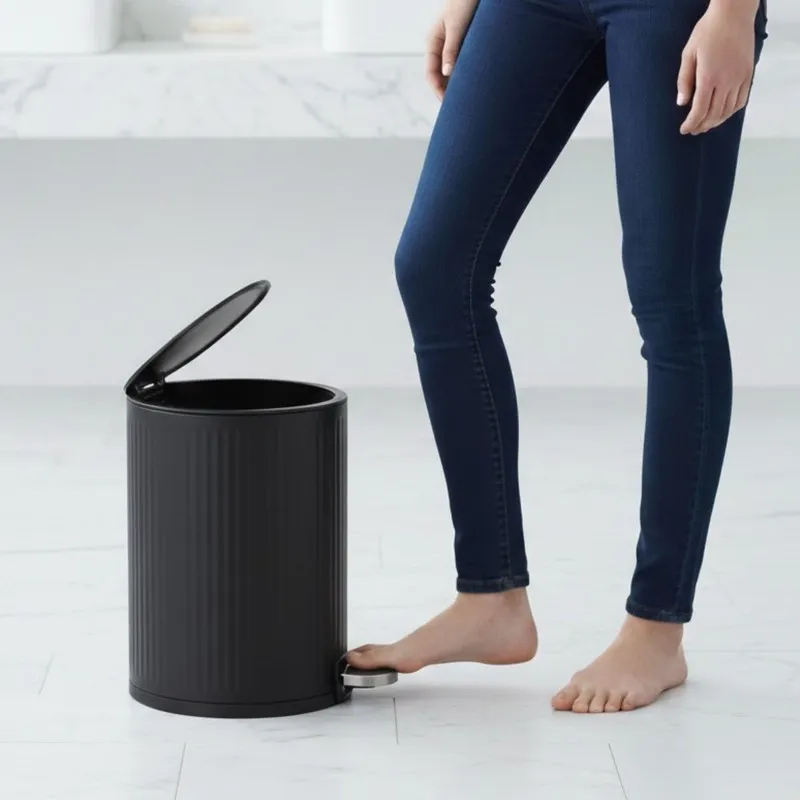 Black pedal dustbin with lid open beside a person
