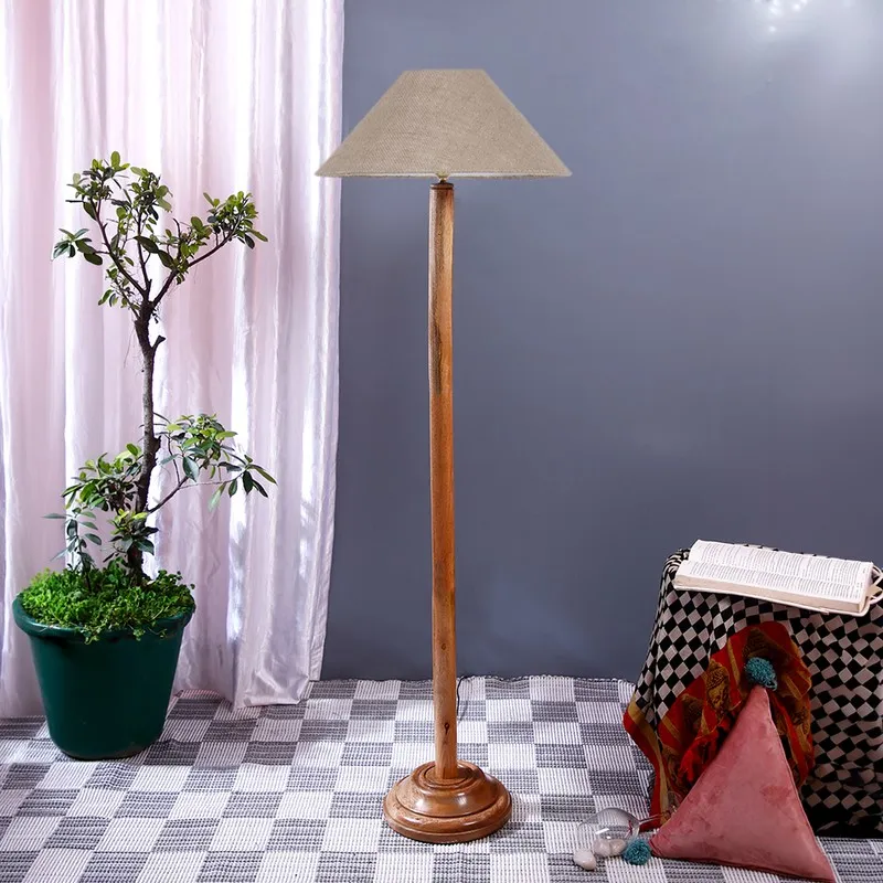 Wooden floor lamp with a beige shade styled beside a potted plant and draped table