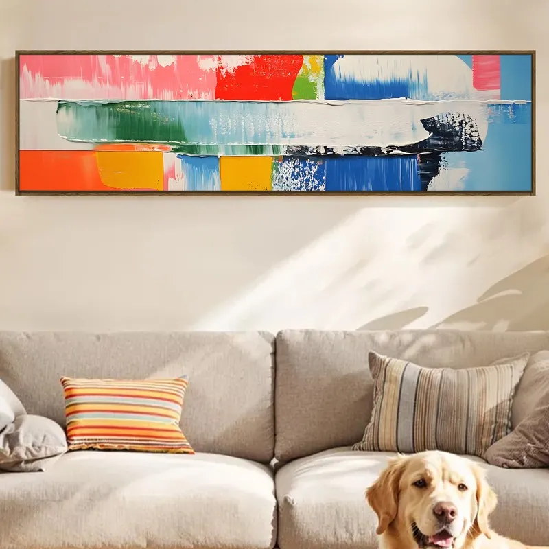 Wide framed abstract canvas in bright colours displayed above a neutral sofa.