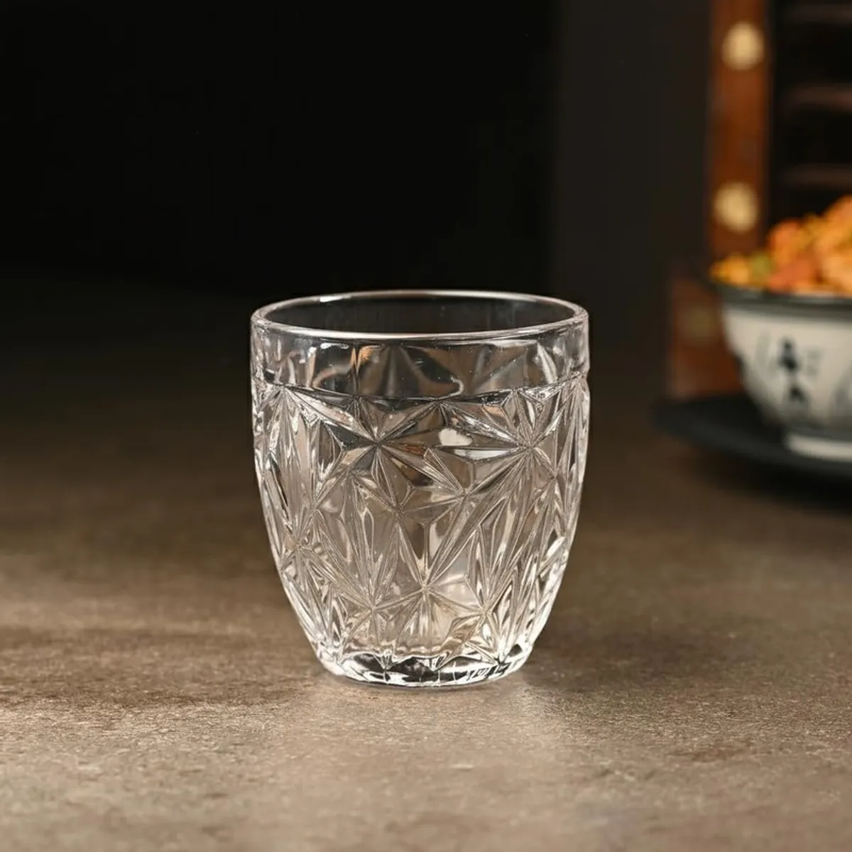 Single clear faceted whiskey tumbler displayed on a neutral tabletop