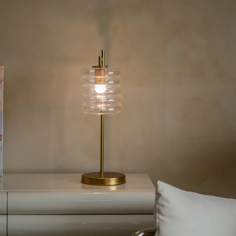 Transparent ribbed glass table lamp glowing on a white bedside table