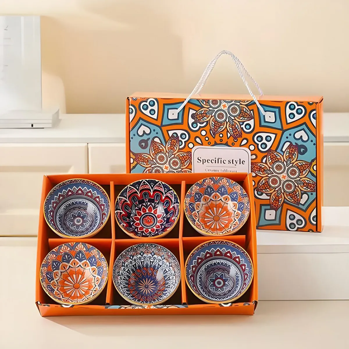 Six colourful mandala bowls arranged in compartments inside an orange presentation box.