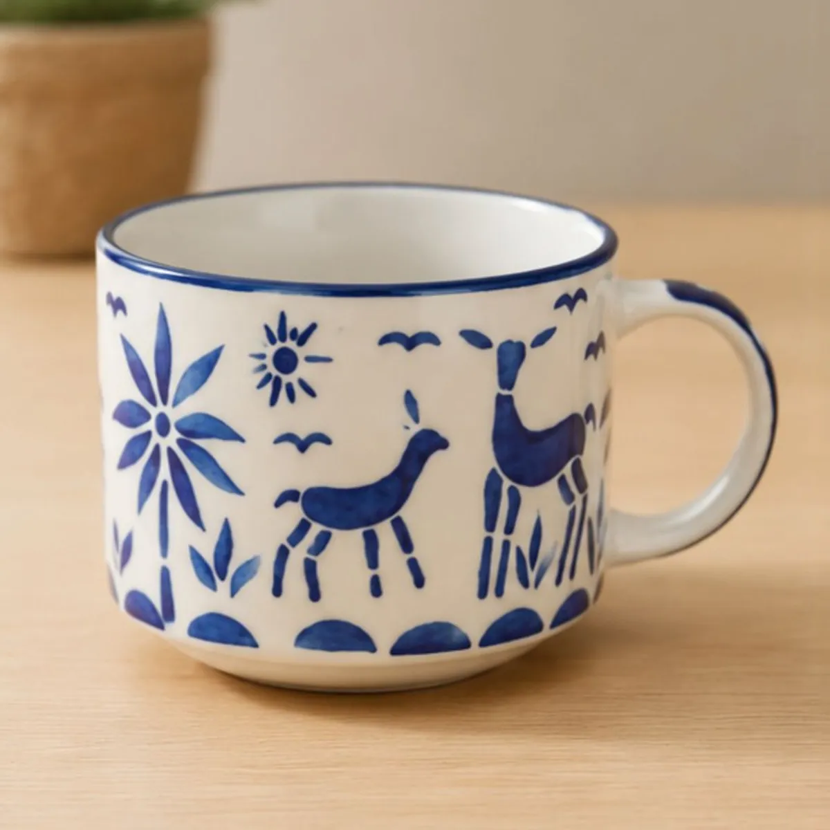 Close-up of a white ceramic cup with blue reindeer, floral motifs and a glossy rim.