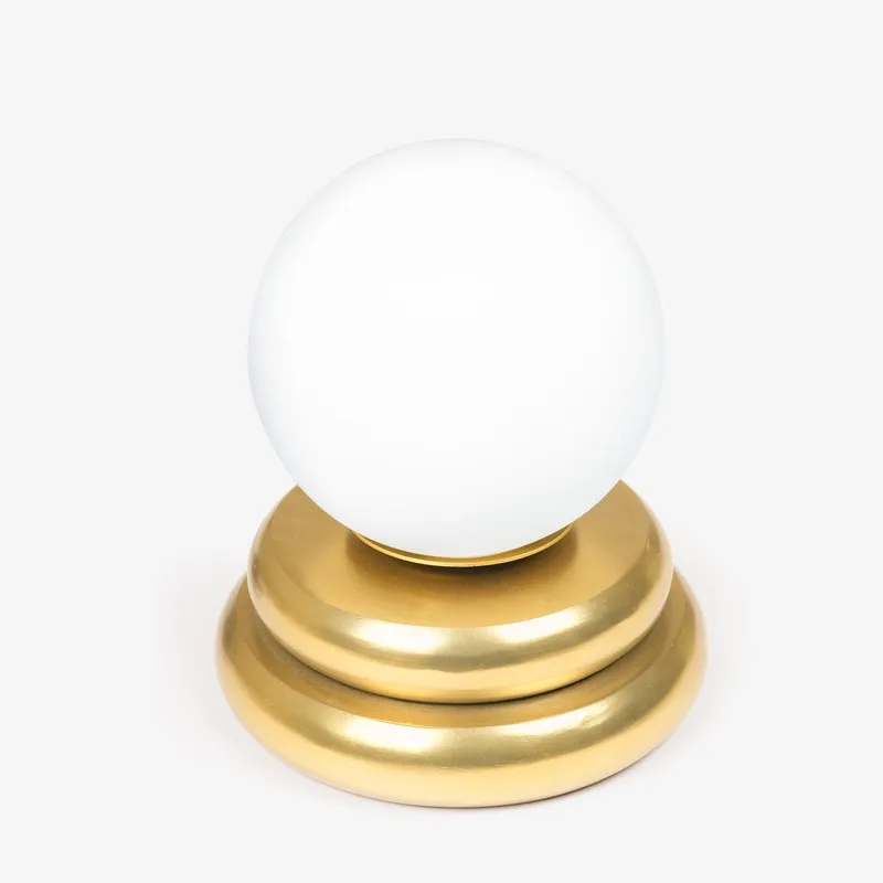 White globe glass table lamp with rounded gold base on a plain background