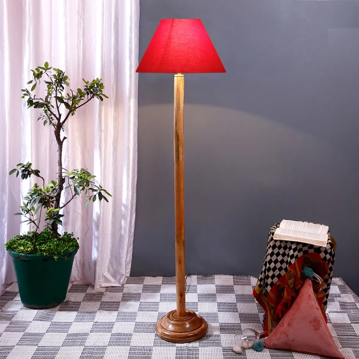 Wooden floor lamp with red conical shade in a styled room with plant and stool