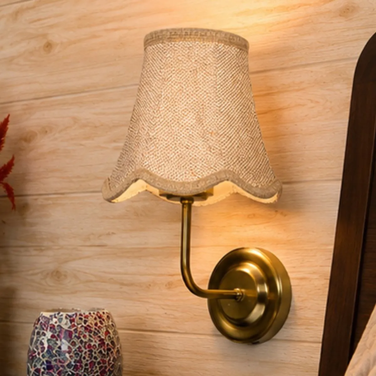 Close view of a beige textured shade and gold-toned wall lamp on a wood-panelled wall