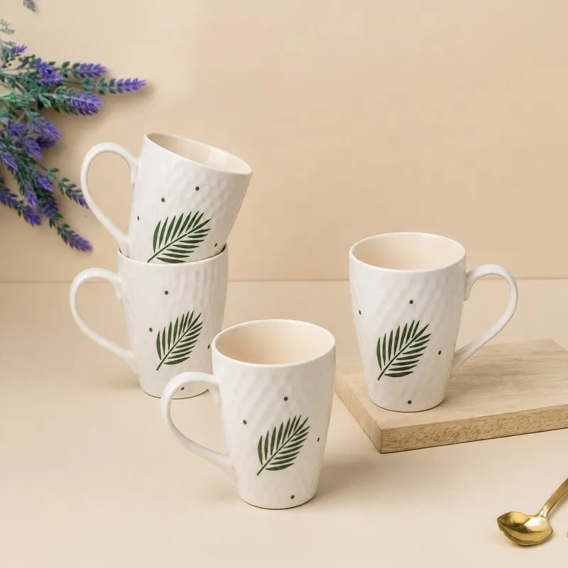 Four white leaf-print mugs arranged on a light wood board