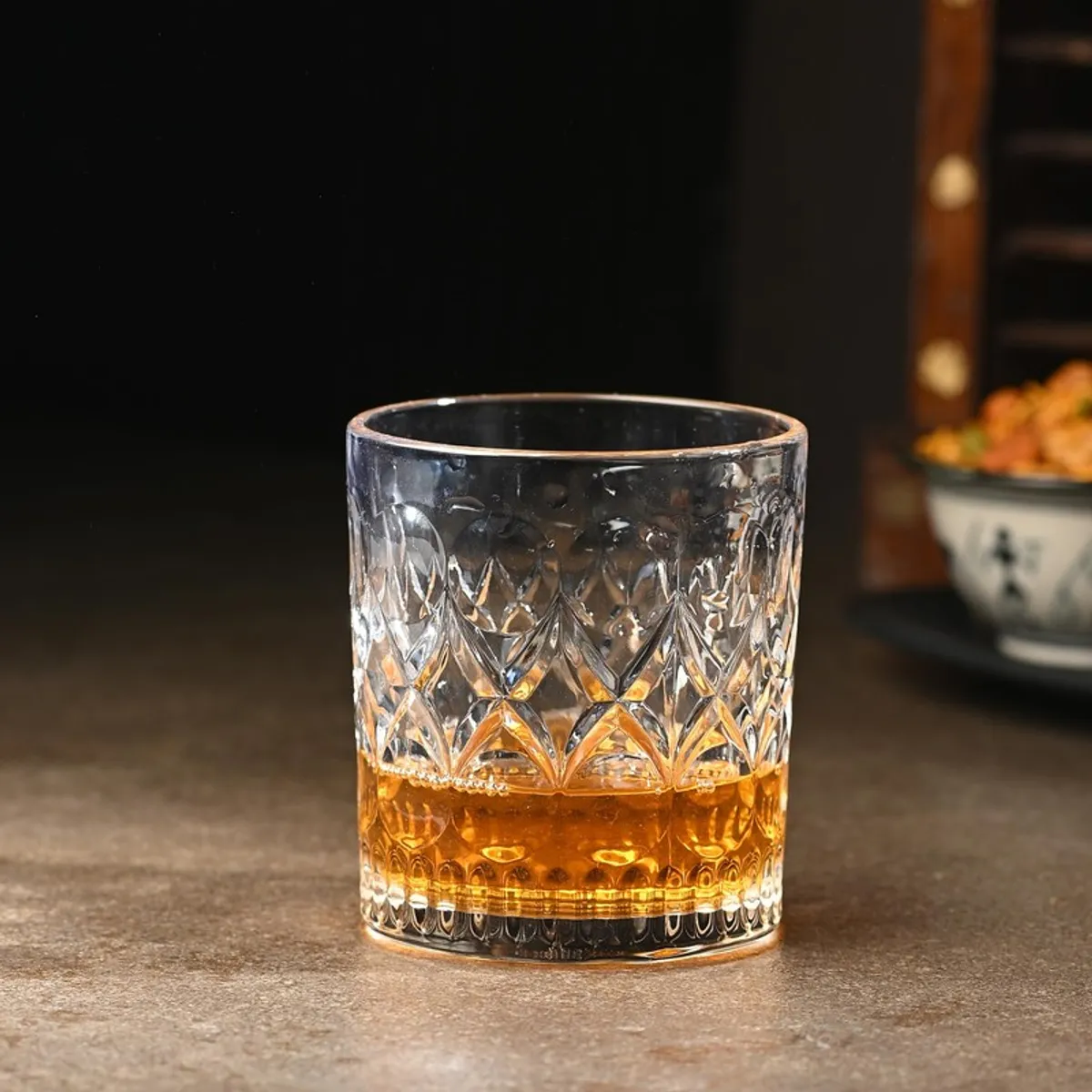 Clear cut-pattern whiskey glass filled with amber whiskey on a dark table