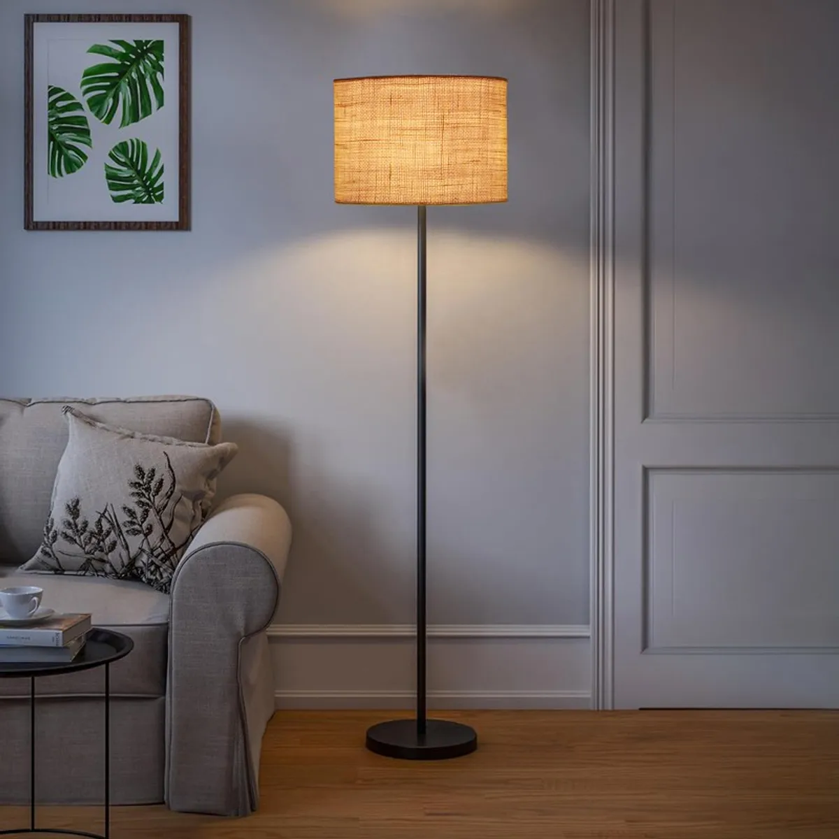 Lit floor lamp with warm shade in a living room corner beside a sofa
