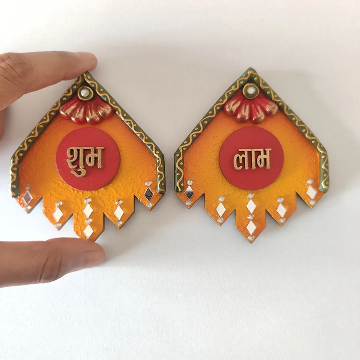 Two small Shubh and Laabh wall accents shown with hand for scale