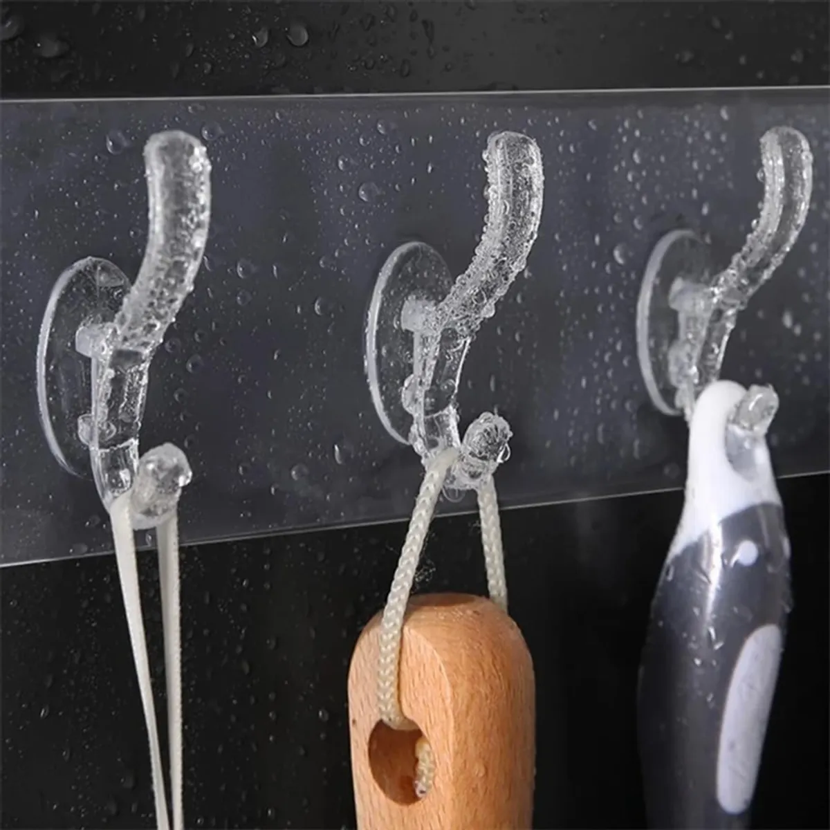 Close-up of transparent hooks mounted on a water-speckled surface