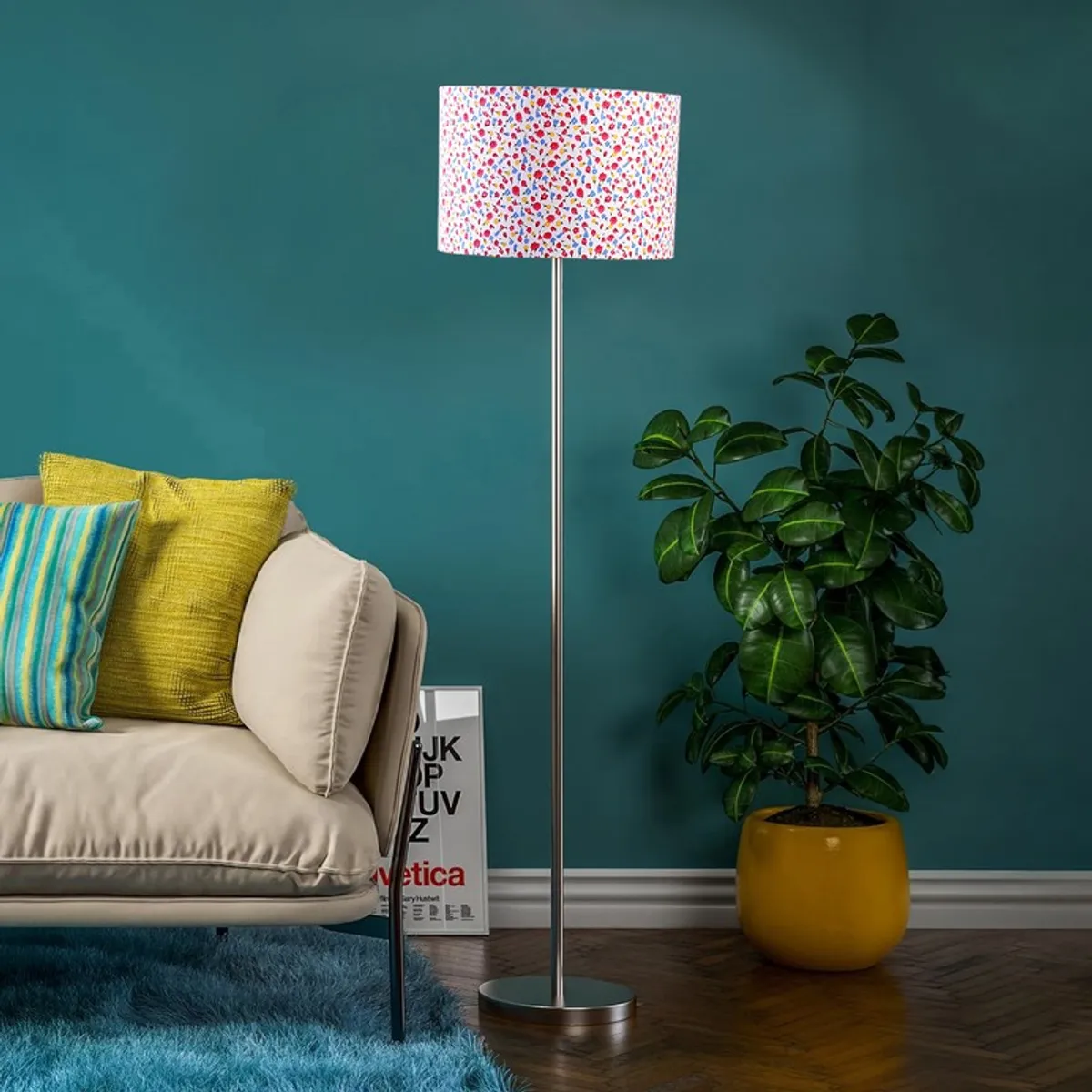 Multicolour drum-shade floor lamp with steel base in a room with teal wall and potted plant