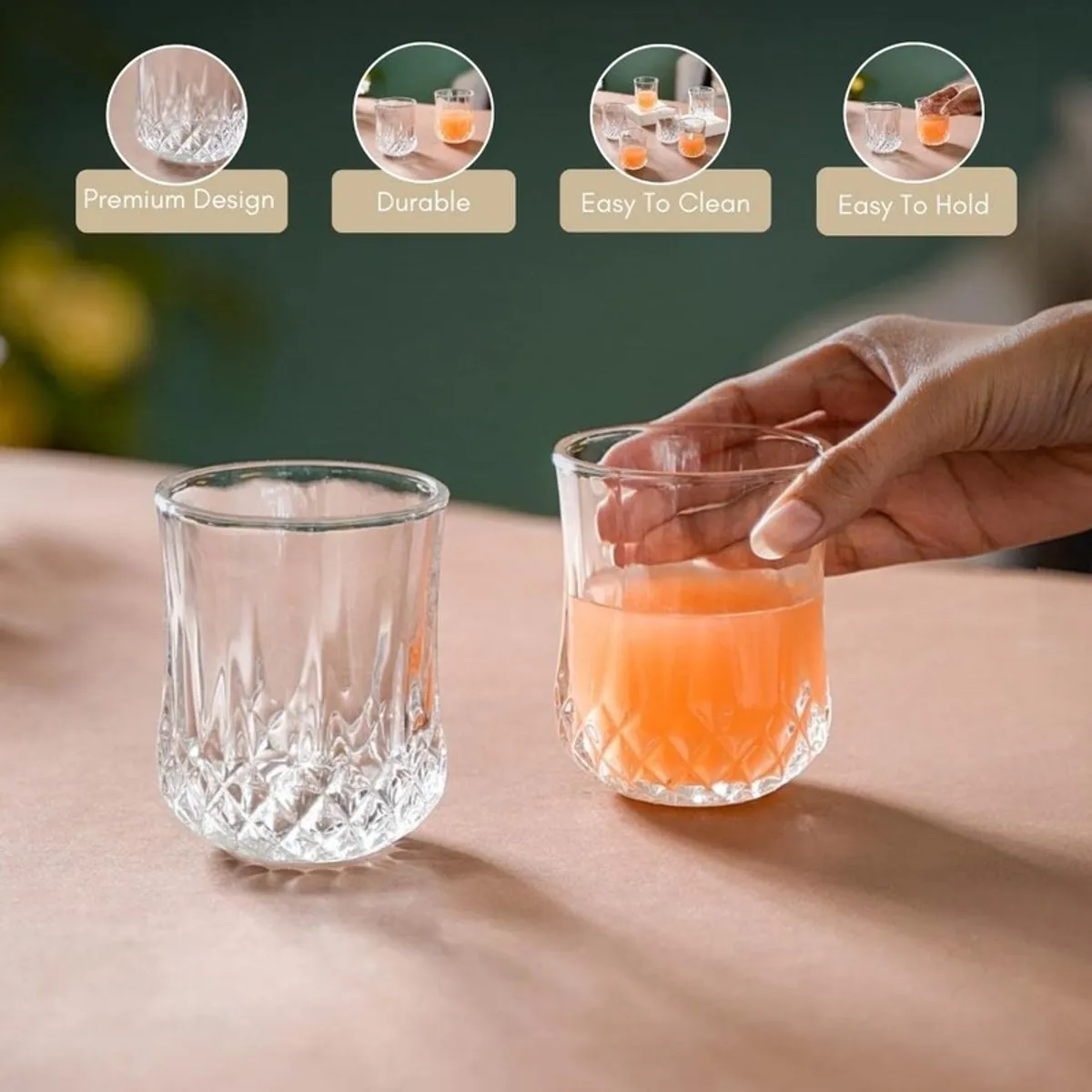 Two clear textured glasses, one filled with orange juice, held on a table