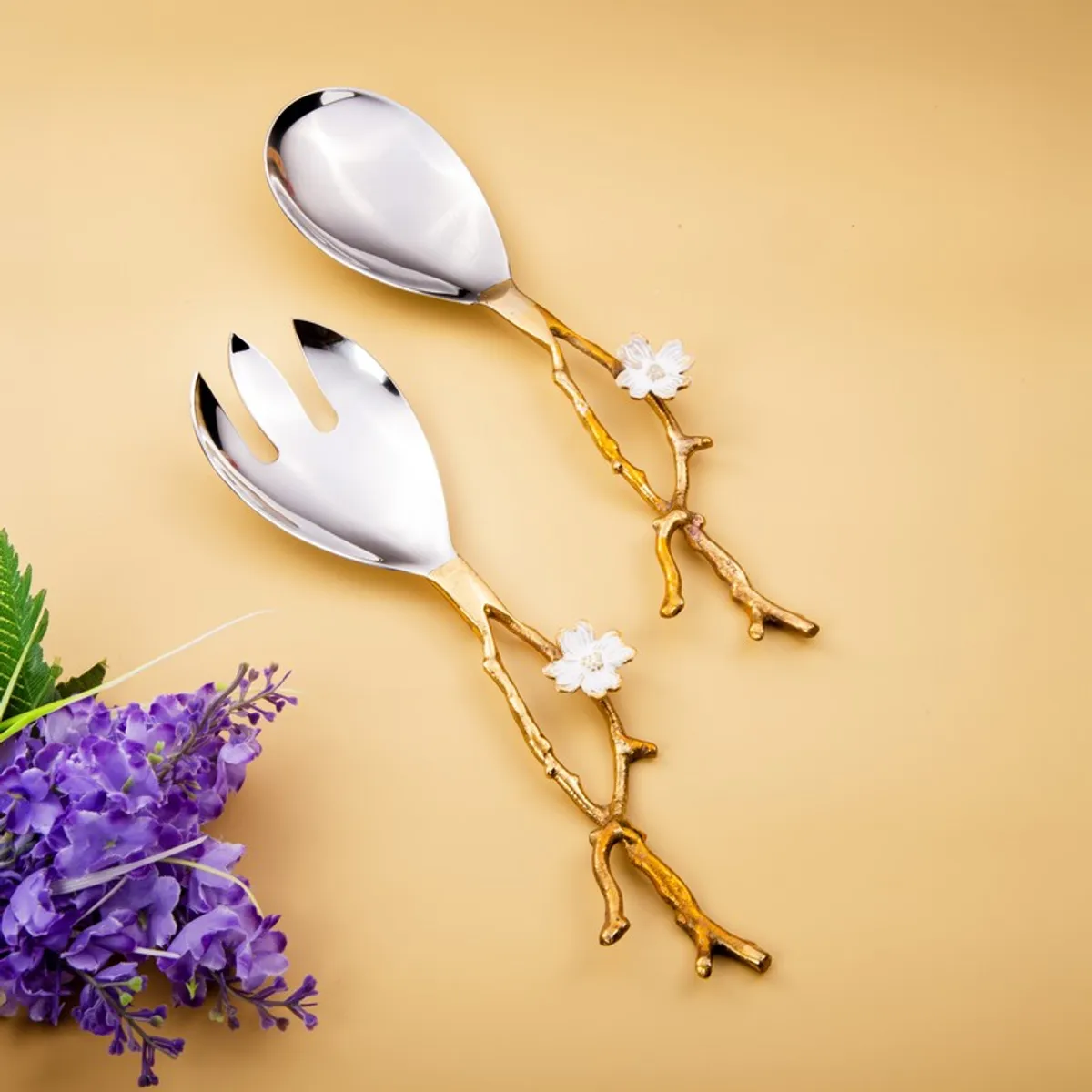 Floral vine salad spoon and fork with silver bowls and gold handles on a warm background.