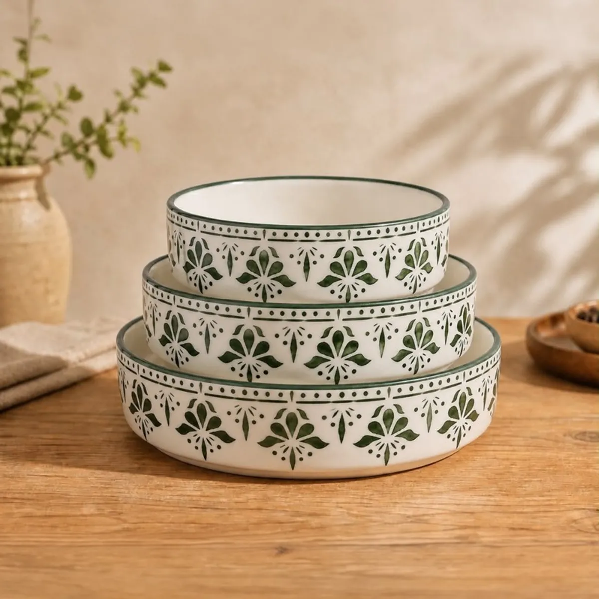 Three white bowls with green floral bands stacked by size on a wooden table