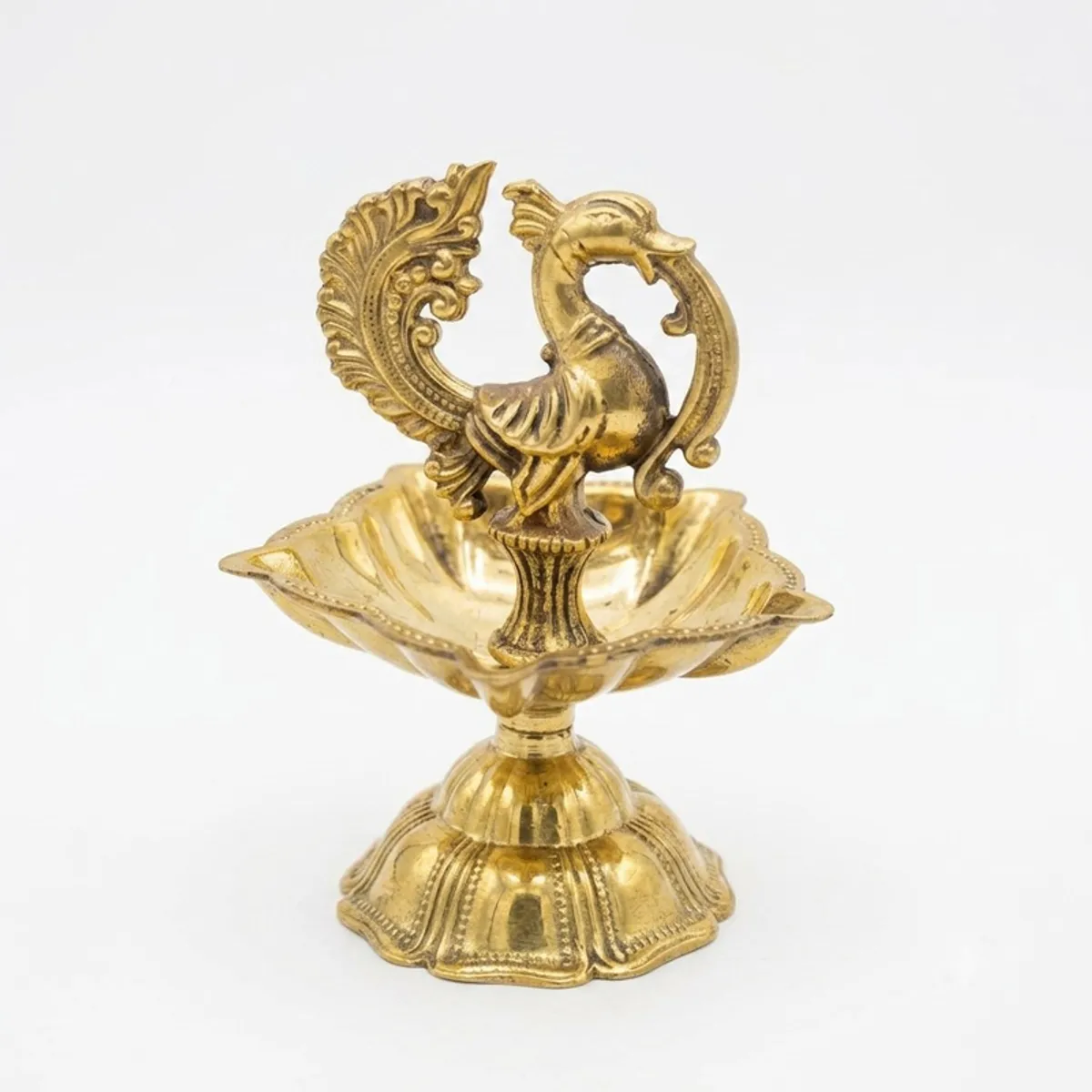 Close-up of a gold brass diya with an intricate peacock design
