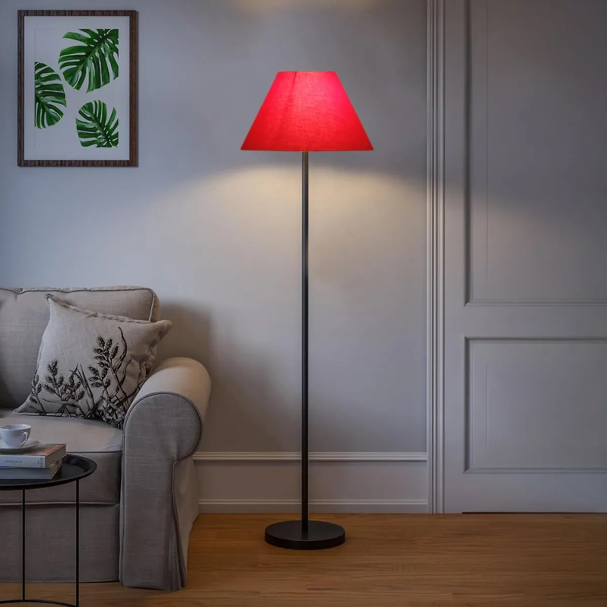 Red floor lamp switched on beside a sofa in a softly lit room.