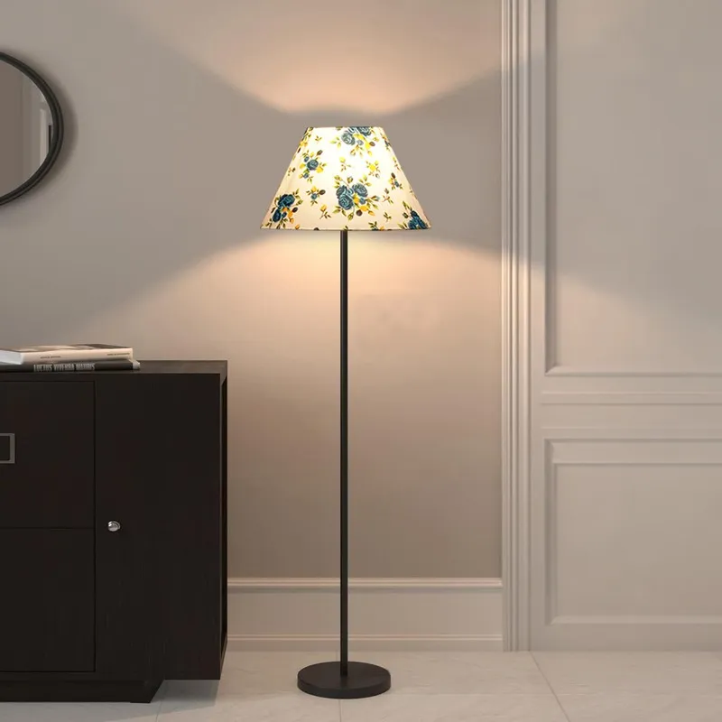 Blue floral shade floor lamp lit beside a dark cabinet against a neutral wall