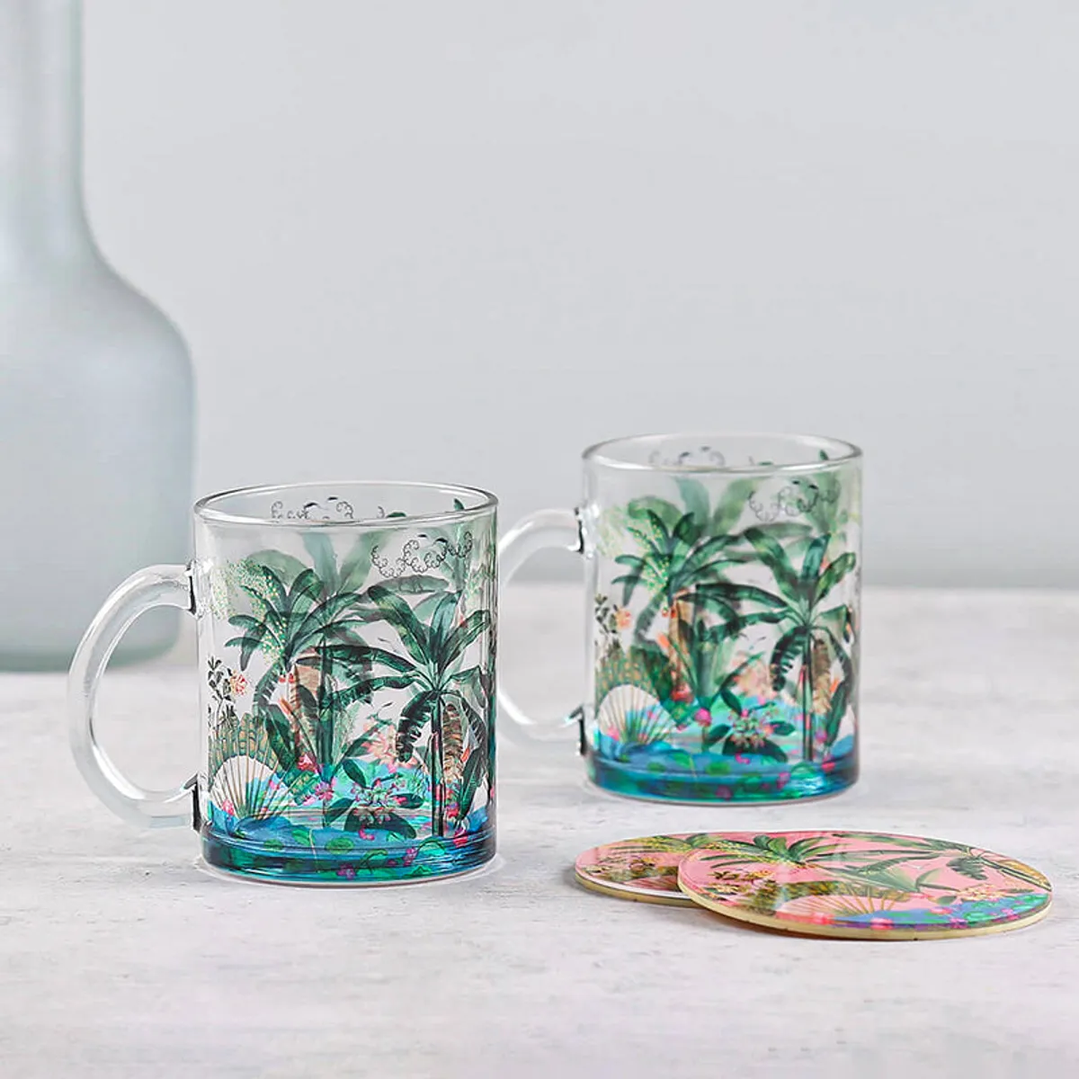 Pair of transparent palm-print glass mugs with colourful tropical coasters