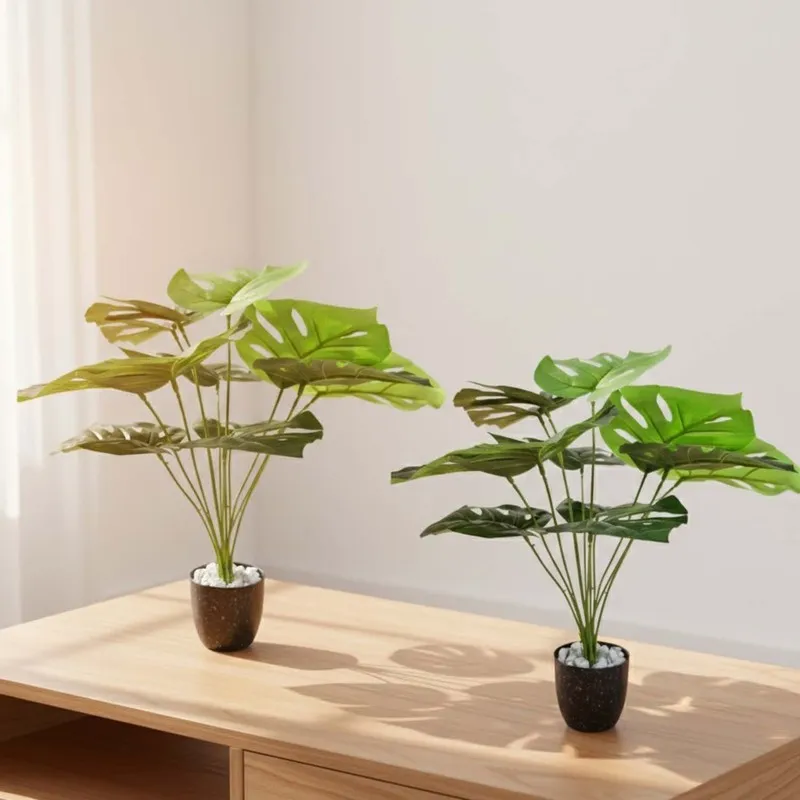 Two artificial Monstera plants in black pots on a wooden table.
