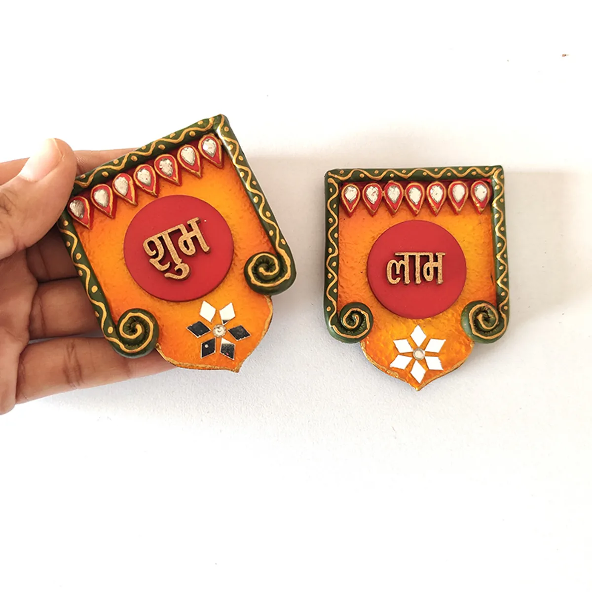 Hand holding one of the two Shubh Labh wall accents for scale