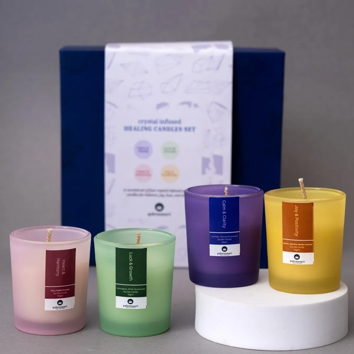 Four cylindrical coloured glass candles arranged in front of their gift box