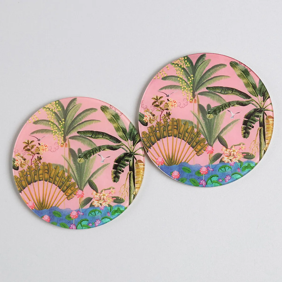 Two round coasters featuring colourful palm and floral artwork
