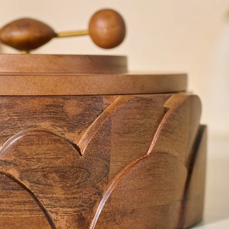 Close-up side view showing the wooden lid, rotating handle and textured carved body.