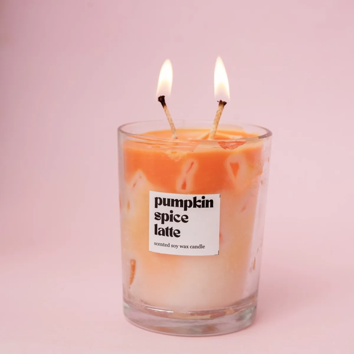 Lit orange-and-cream pumpkin spice candle with two wicks in a glass jar