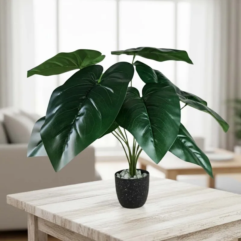 Single faux green leafy plant in a black pot displayed on a light wood table.