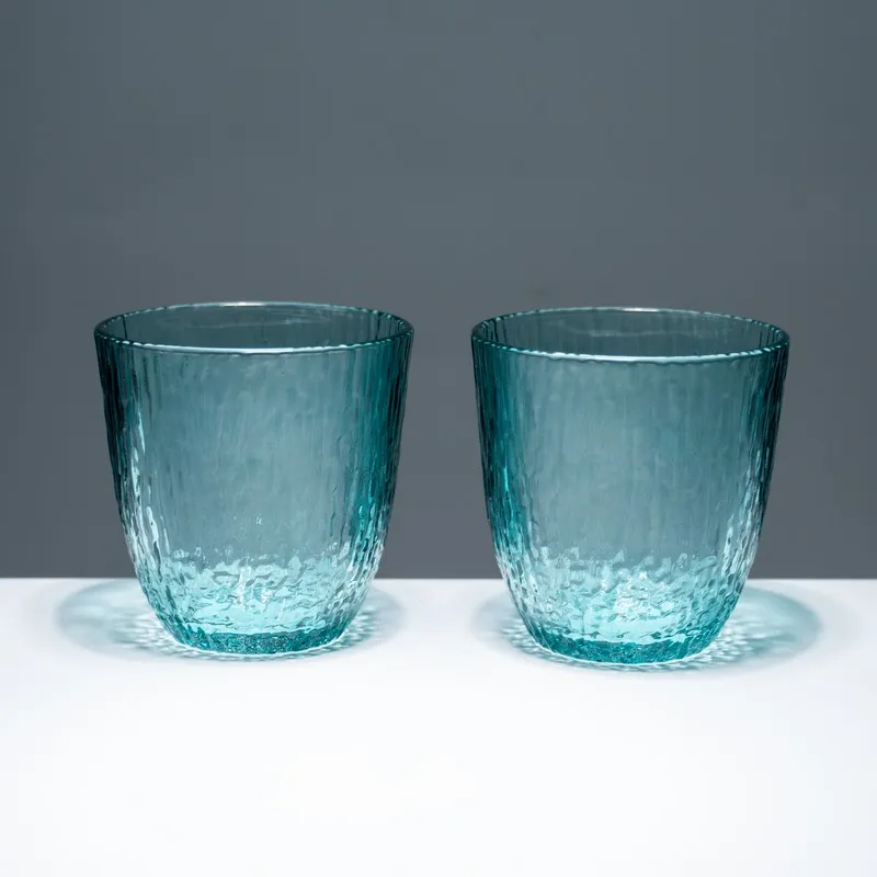 Two blue tinted textured drinking glasses on a white surface