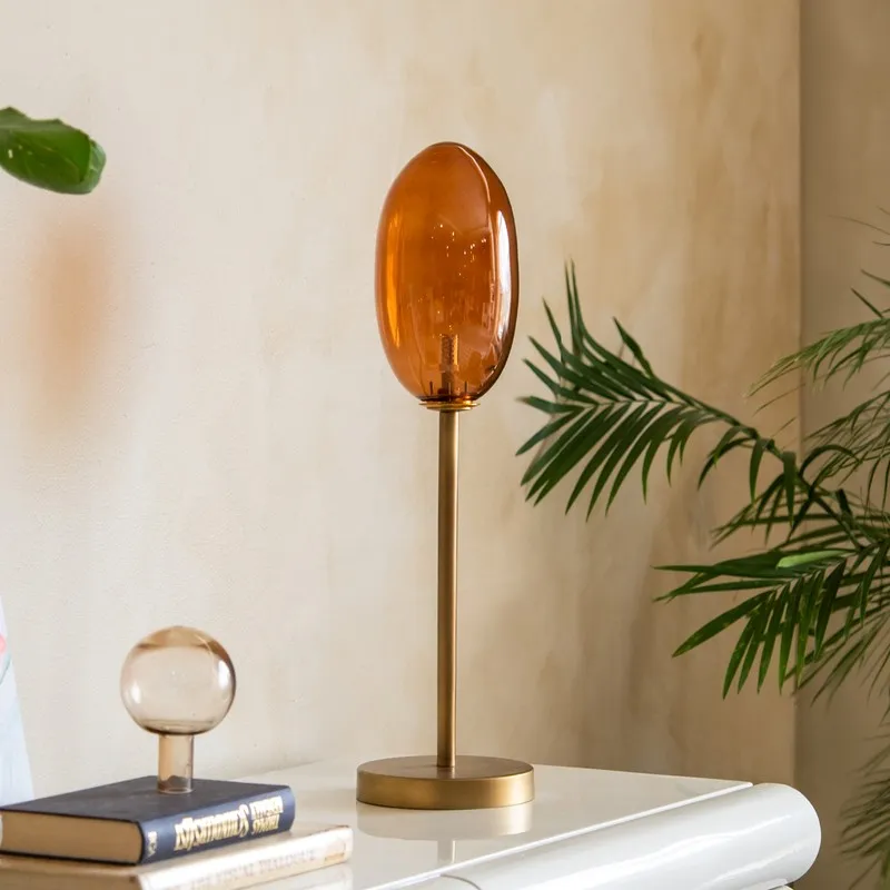 Amber glass table lamp with slim gold-toned stand on a white console