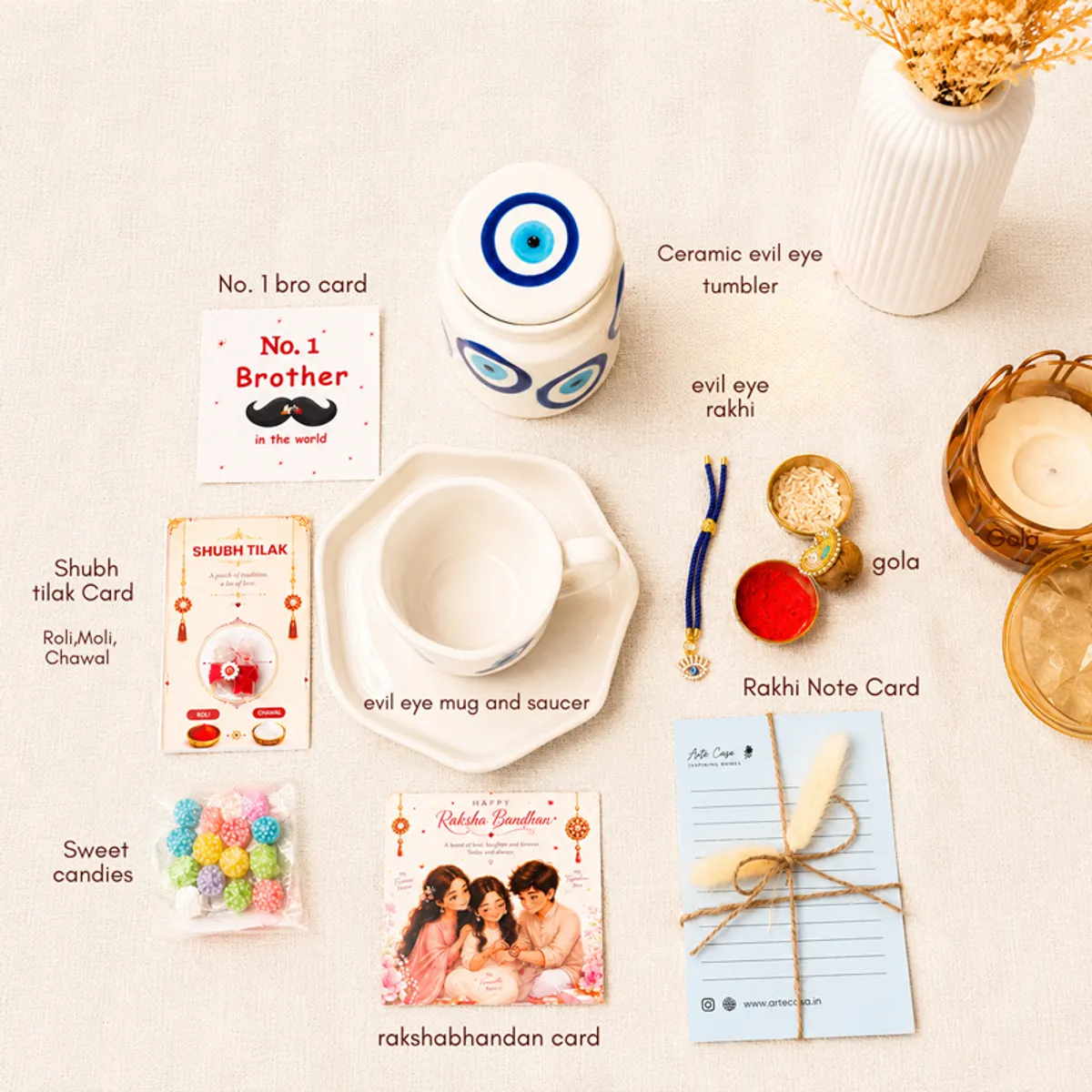 Hamper contents arranged separately, including blue evil eye drinkware, cards, Rakhi and sweets