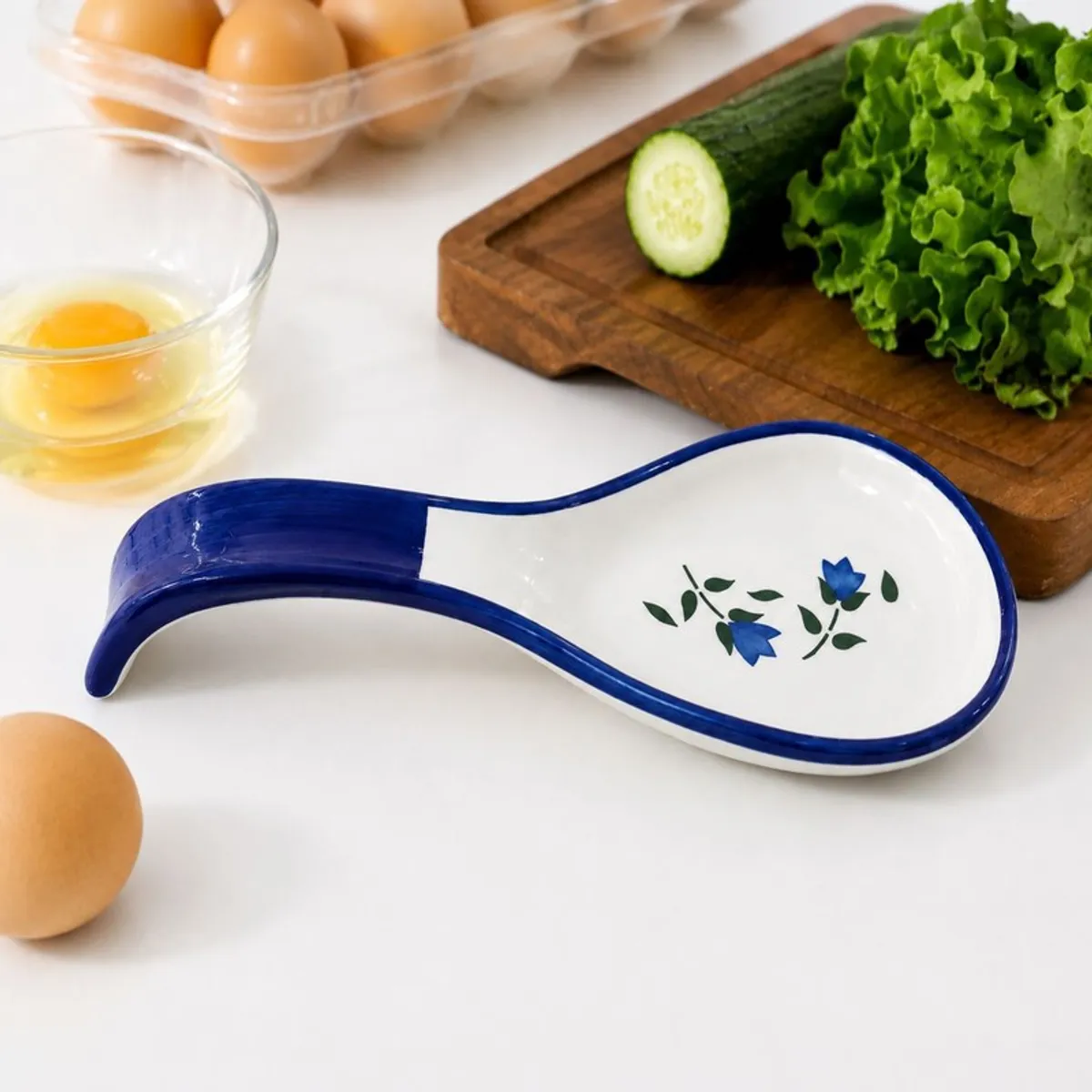 Blue ceramic spoon rest with floral motif beside vegetables and a bowl