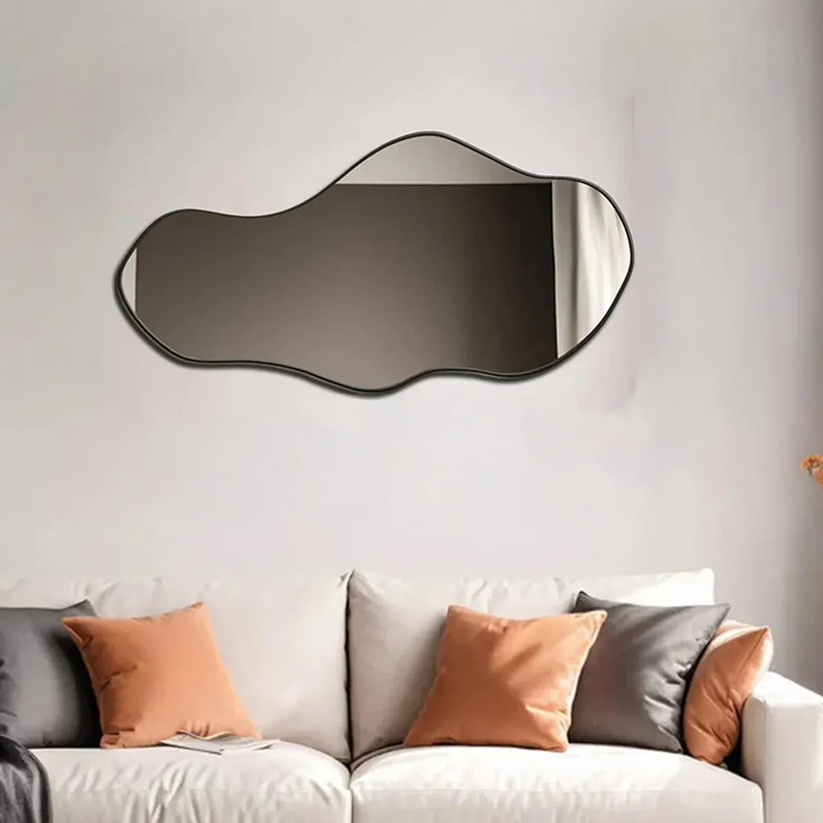 Free-form wall mirror with black edging above a light sofa