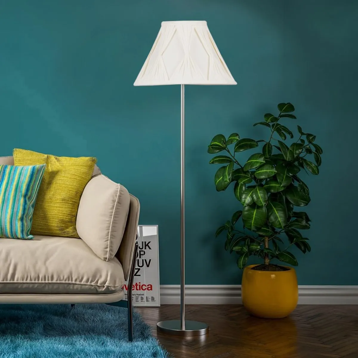 White tapered floor lamp with slim metal stand against a teal wall beside a sofa and plant
