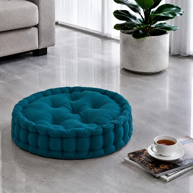 Botanical green round floor cushion styled on a polished floor beside a plant and books.