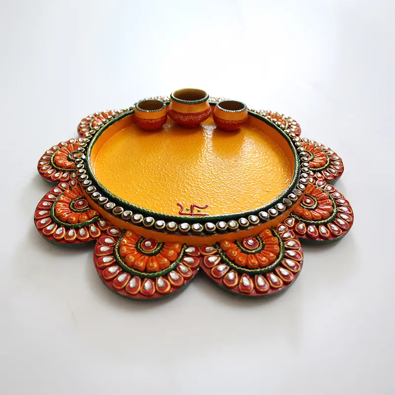 Round yellow pooja plate with ornate orange floral edge and three bowls on a white background