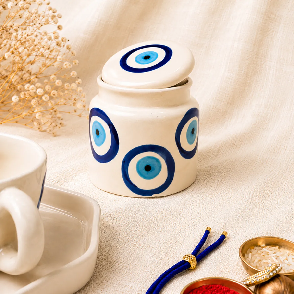 Close-up of white evil eye jar with blue circular motifs beside a Rakhi