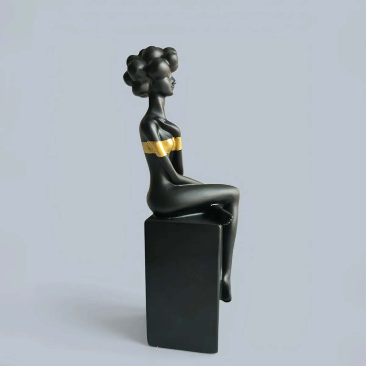 Side view of a black and gold sitting lady figurine on a rectangular base