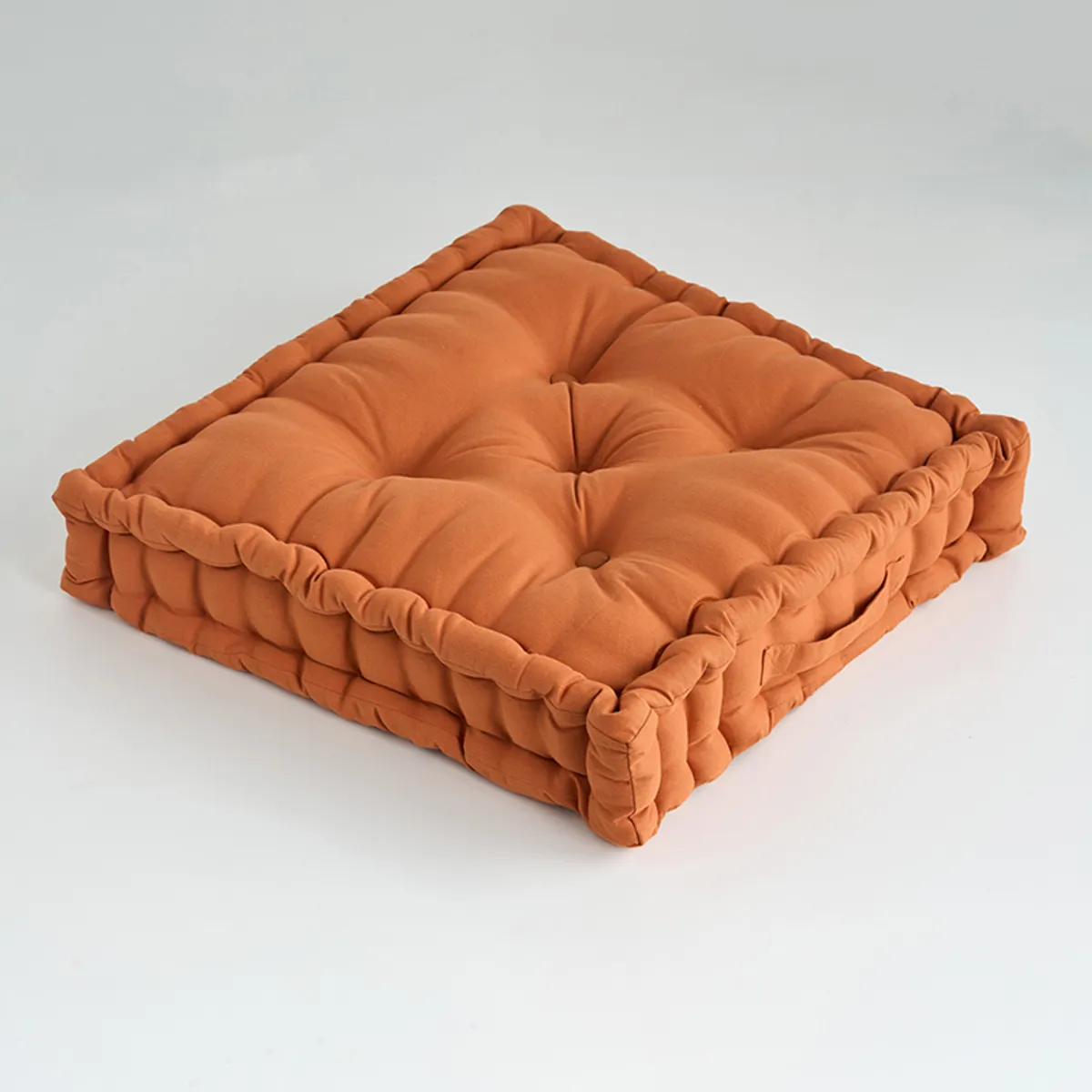 Close-up of a square tufted floor cushion with a softly gathered border and button details.