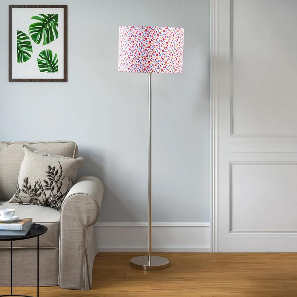 Multicolour drum-shade floor lamp with steel base beside a sofa in a bright room