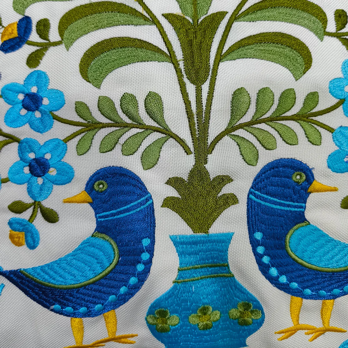 Close-up of blue embroidered birds, flowers and green foliage on a cushion cover