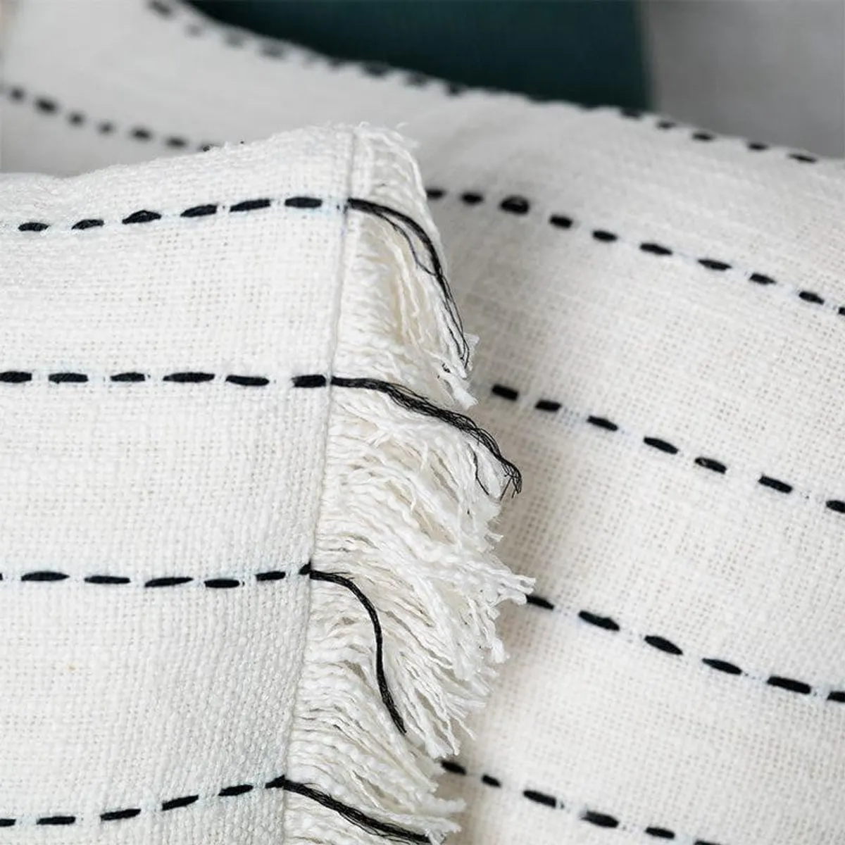 Close-up of white cushion cover fabric with black stripes and fringed edge