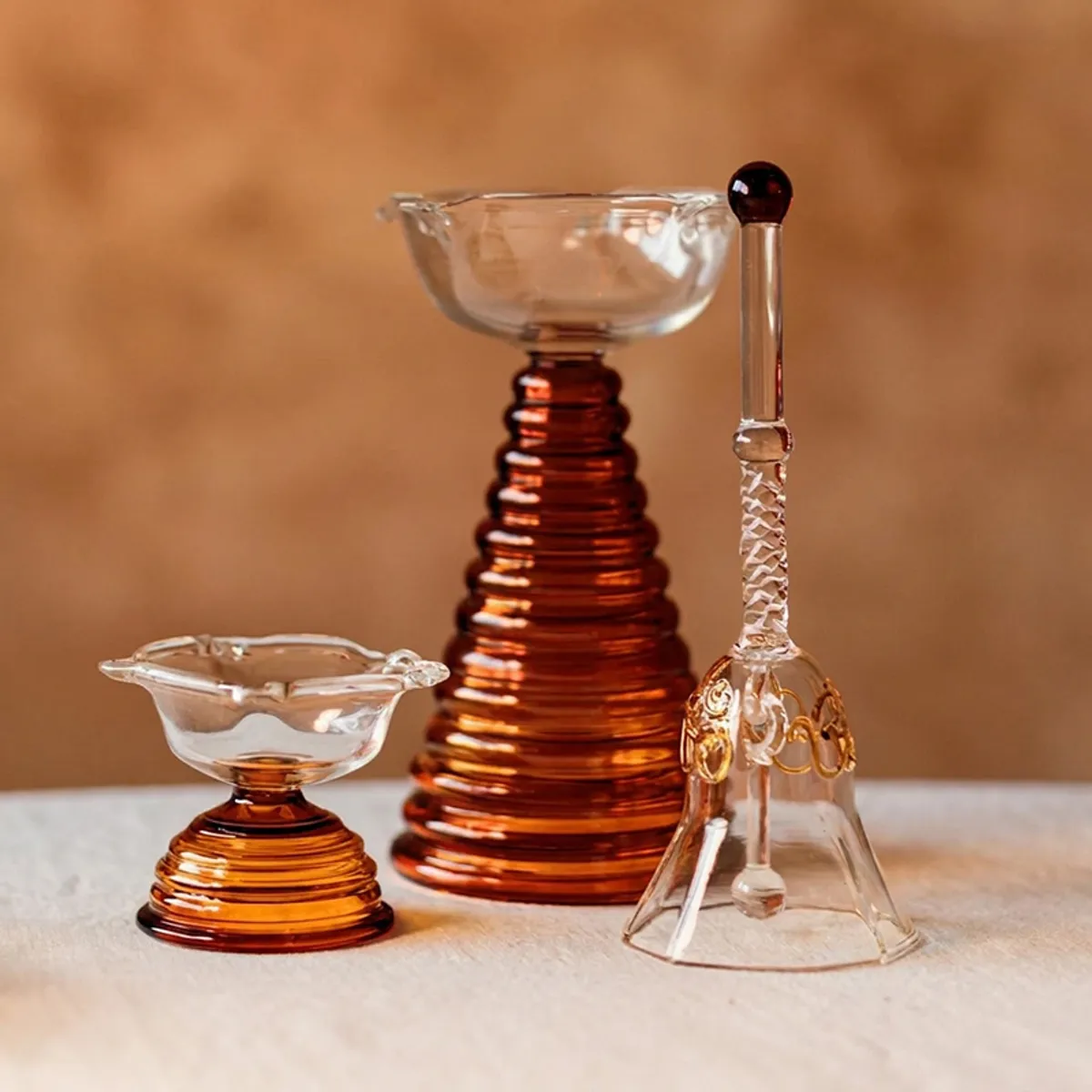 Three-piece brown and transparent glass pooja set displayed together